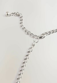 Silverfärgad metallkedja med länkar som har en polerad yta. Inkluderar en rund metallboll som accent och ett lås.
