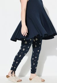 Abito blu navy con orlo svasato abbinato a leggings blu navy con motivi geometrici crema, completato da sandali leggeri comodamente indossabili.