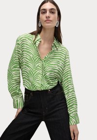 Groen en wit gestreepte button-up shirt met lange mouwen, voorzien van een kraag en een ontspannen pasvorm, gecombineerd met donkere spijkerbroek.