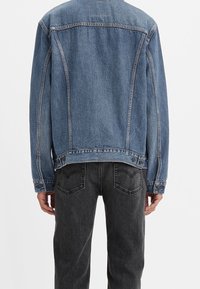 Denim jacket in light blue with a relaxed fit, featuring two chest pockets and button accents. Paired with dark gray jeans.