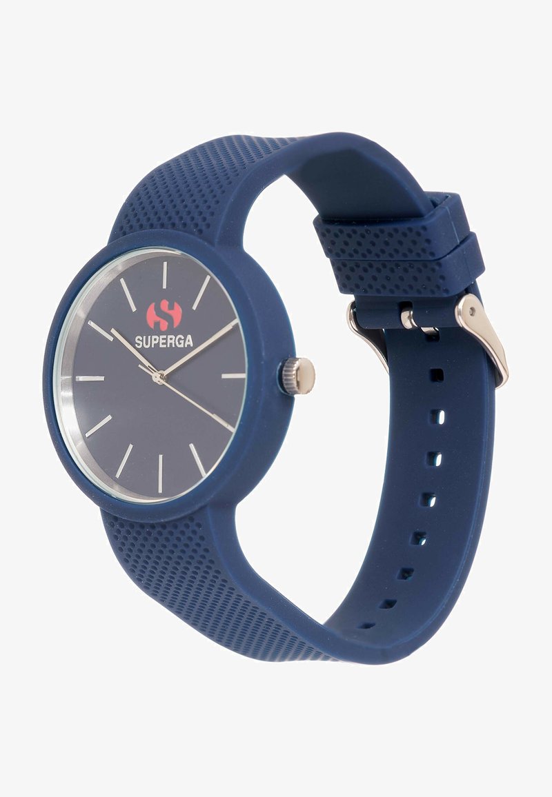 Sinine silikoonkell ümmarguse kupliga, hõbedaste aktsentidega, tekstuuriga rihmaga ja selge puutega, kus on valged tunni markerid ja punane logo.