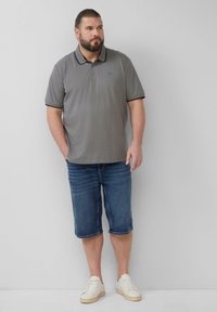 Szara koszulka polo z czarnym wykończeniem, zestawiona z niebieskimi szortami dżinsowymi do kolan. Model w białych trampkach, stojący na jasnym tle.