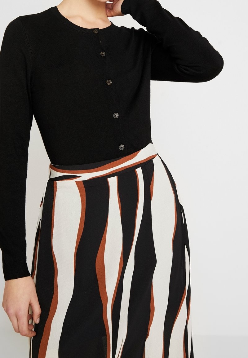 Svart stickad cardigan med lång ärm och knäppning fram, kombinerad med en randig kjol i beige, svart och brunt.