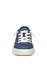 Marineblauwe canvas sneakers met witte veters, gestructureerde zool en gestikte details. Merklabel zichtbaar op de tong, afgeronde teenvorm.