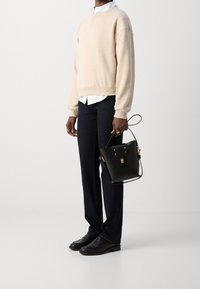 Suéter beige, camisa blanca debajo, jeans oscuros, bolso negro con herrajes dorados y zapatos de cuero negros. Diseño limpio y minimalista.