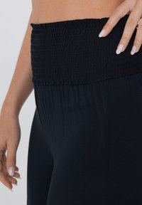 Leggings noirs avec une taille smockée, présentant une texture lisse et un design ajusté, mettant en avant un tissu doux et des détails plissés subtils.