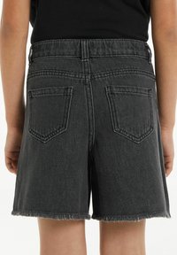 Černé džíny šortky s třepícími se okraji, obsahující dvě zadní kapsy a žebrovaný pas. Materiál má pevnou strukturu.