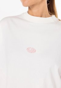 Baltas apvalaus kaklo džemperis, ant krūtinės turintis mažą rožinės spalvos "PEGADOR" logotipą. Minkšta medžiaga, laisvas pjūvis ir minimalūs siuvimo detalės.