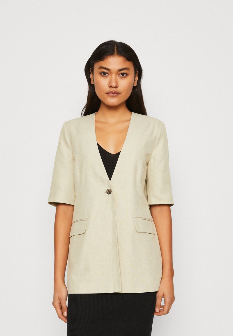 Beige blazer med djup V-halsringning, korta ärmar, en knappstängning och två framfickor. Slät tyg med en subtil textur.