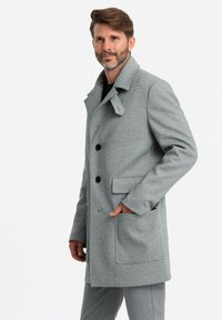 Abrigo de lana gris con textura de espiga, que presenta un frente de doble botonadura, grandes botones negros y bolsillos laterales.