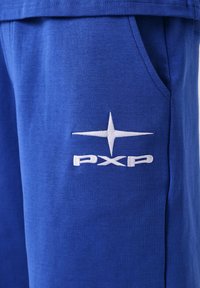 Pantalon en tissu bleu avec un logo blanc en forme d'étoile et le texte « PXP » brodé près de la poche latérale.