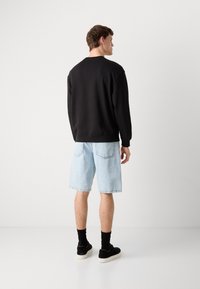 Zwarte sweatshirt met ronde hals, gecombineerd met lichtblauwe denim short en zwarte schoenen. Kenmerken zijn ribgebreide manchetten en achterzakken.
