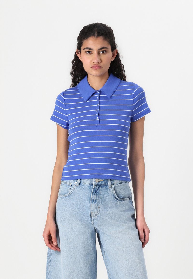 Chemise polo bleue avec des rayures horizontales blanches, à manches courtes et col, dotée d'un boutonnage. Associée à un jean large bleu clair.