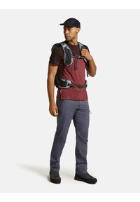 Conjunto de senderismo que incluye una camisa de manga corta en color burdeos y negro, mochila gris, pantalones grises y botas de senderismo negras con detalles en azul.
