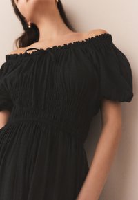 Schwarzes, schulterfreies Kleid mit gerafftem Oberteil und Puffärmeln; fließender, strukturierter Stoff; minimalistisch gestaltet; leichter Look.