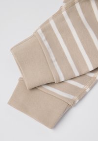 Beige katoenen kledingstuk met witte strepen, met een zachte textuur. De mouwen zijn geribbeld en afgewerkt voor duurzaamheid. Over het algemeen een gladde afwerking.