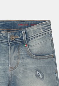 Szorty dżinsowe z wyblakłym wykończeniem, przetartą łatą na udzie, przednią kieszenią, metalowym guzikiem oraz małą flagą włoską przy kieszeni.