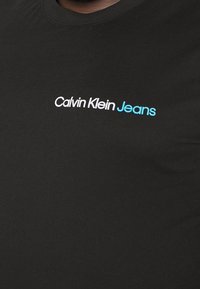 T-shirt nera con colletto rotondo, con il logo "Calvin Klein Jeans" in bianco e blu. Realizzata in morbido tessuto di cotone.