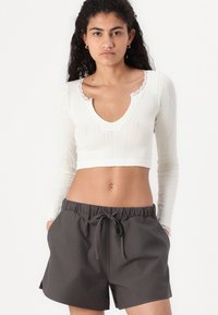 Top scurt alb cu dungi, având un guler dantelat, combinat cu pantaloni scurți elastici gri închis cu șnur, care au buzunare laterale.