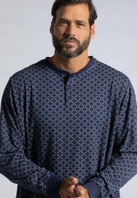Maglietta a maniche lunghe blu navy con stampa geometrica a rombi, dotata di colletto rotondo e tre bottoni viola al collo. Tessuto morbido, vestibilità casual.