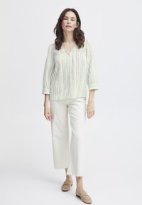 Blusa leggera a righe con scollatura a V, bottoni frontali e maniche a tre quarti in verde pastello e crema. Abbinata a pantaloni bianchi a gamba larga.