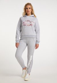 Grijze hoodie met glanzende roze tekst en grijze joggers met een wit logo. Zachte stof met geribbelde boorden en tailleband. Casual sportkleding.
