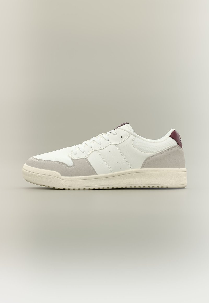 Λευκό αθλητικό παπούτσι χαμηλού προφίλ με μπεζ σόλα, γκρι σουέτ διακοσμητικά, λευκά κορδόνια και σκουρό κόκκινη πίσω ταμπέλα σε ουδέτερο φόντο.