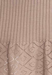Beige gestrickter Stoff mit vertikaler Rippung oben und einem rautenförmigen Spitzenmuster unten.