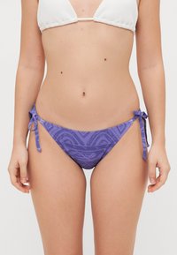 Fialové bikiny s viazaním po stranách, s komplexným abstraktným vzorom a hladkou textúrou. Ozdobené malými okami na prispôsobenie.