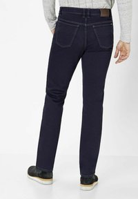 Dark blue denim jeans with a straight-leg design, rear pockets, and a leather patch on the waistband. Slim fit and smooth texture.