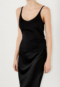 Sort satin cami med tynde stropper og v-hals-design, parret med en matchende satin-nederdel. Glat tekstur, tætsiddende silhuet.
