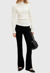 Valkoinen, teksturoitu pitkähihainen paita yhdistettynä mustiin leveälahkeisiin housuihin ja mustaan laukkuun; vaatteiden kanssa on litteät kengät, joissa on kultaisia yksityiskohtia.