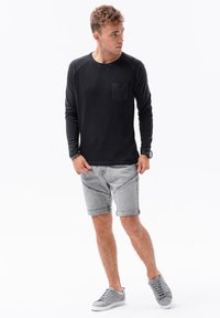 Svart långärmad skjorta med en bröstficka, tillsammans med ljusgrå shorts och grå sneakers, med uppvikt ärm och en strukturerad tyg.