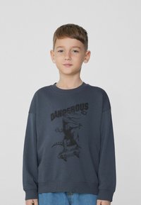 Tmavě modrá mikina s dlouhými rukávy, s černou grafikou dinosaura a textem "DANGEROUS REX" na textu s hladkým, strukturovaným povrchem.