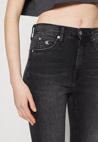 Vaqueros negros de mezclilla con corte ajustado, diseño de cinco bolsillos y un pequeño logo CK en el bolsillo delantero. La textura es suave con un ligero desgaste.