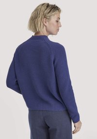 Lila Strickpullover mit strukturiertem Finish, Rundhalsausschnitt und Rippenbündchen, kombiniert mit dunkelblauen Hosen, von hinten betrachtet.