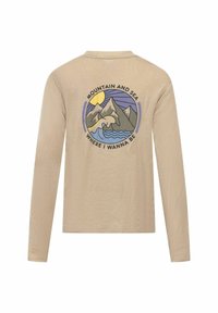 Beige overhemd met lange mouwen, voorzien van een cirkelvormige graphic van bergen en golven met de tekst "BERG EN ZEE WAAR IK WIL ZIJN".