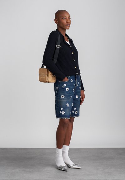 Marineblauwe geribbelde cardigan met gouden knopen, denim shorts met witte bloemenborduursels, zilveren ballerina's en witte sokken. Schoudertas met tekst.