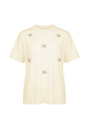 Kremowy T-shirt z krótkim rękawem z sześcioma małymi różowymi haftowanymi kokardkami rozmieszczonymi z przodu. Brak widocznych logo ani innych wzorów.