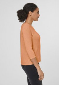 Oranje gebreide top met driekwartmouwen, ronde halslijn en een rechte zoom, gecombineerd met zwarte strakke broek. Zachte textuur.