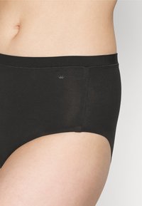 Slip in cotone nero con una texture liscia, vita elastica e un piccolo logo a corona sul lato. Design semplice con copertura totale.