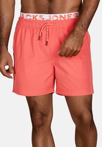 Pantaloni da nuoto corallo realizzati in tessuto leggero, con una vita elasticizzata e coulisse, e un bordo bianco con logo. Design casual.