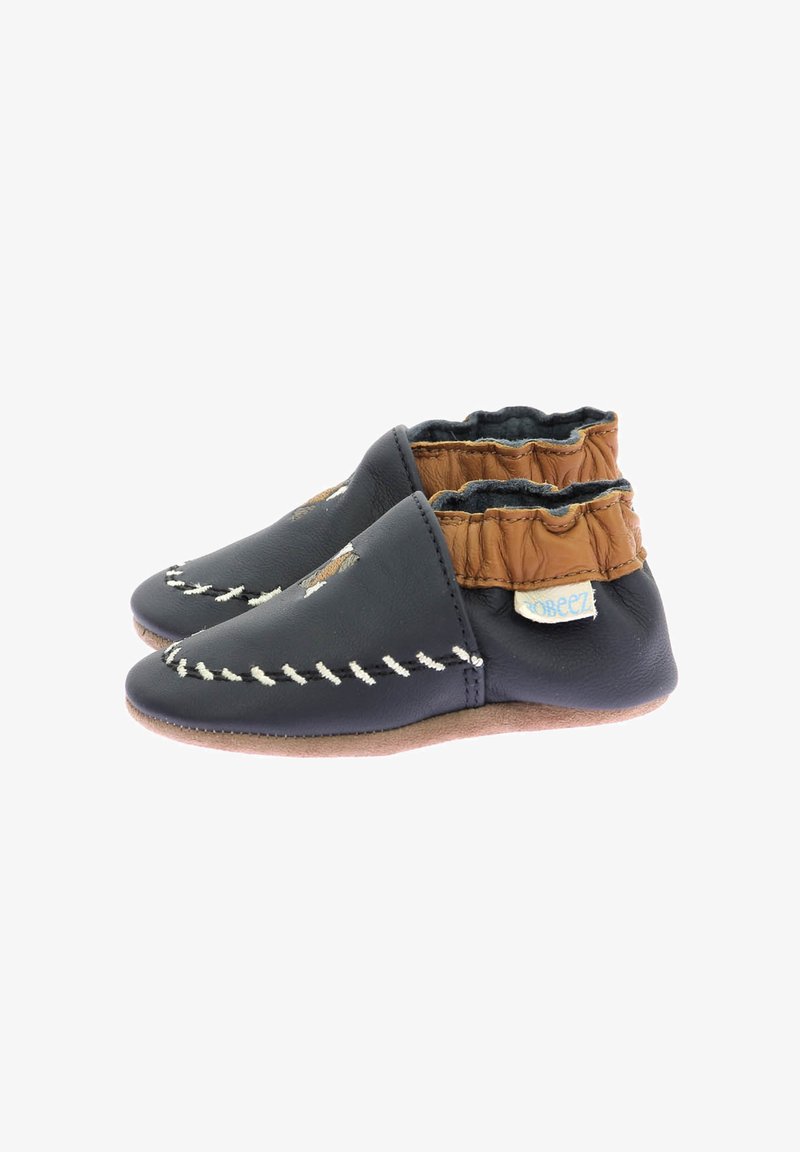 Chaussures en cuir pour bébé avec une surface bleu marine, un bracelet élastique couleur beige et des coutures blanches. Semelle souple pour flexibilité et confort.