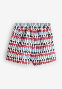 Mönstrade badshorts med en upprepad design av soldater i röda jackor och höga svarta hattar, mot en ljusblå bakgrund.