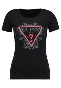 Svart t-shirt med kort ärm som har en rosa triangulär logotyp med texten "GUESS U.S.A" och grå blommönster som omger den.