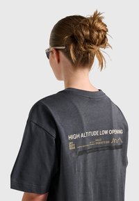 Ciemnoszary bawełniany t-shirt z nadrukiem na plecach w żółtym kolorze. Luźny krój, krótkie rękawy i okrągły dekolt.