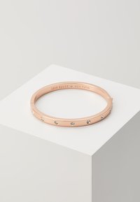 Rose gold bangle bracelet featuring evenly spaced clear rhinestones along the outer surface. Engraved brand name inside the band.