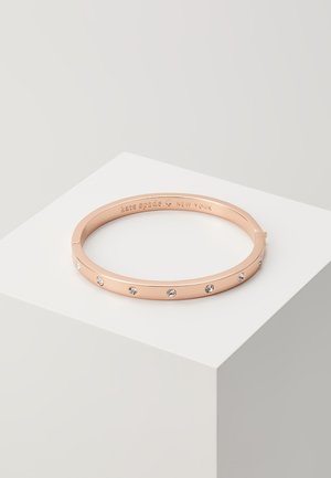 Rose gold bangle bracelet featuring evenly spaced clear rhinestones along the outer surface. Engraved brand name inside the band.