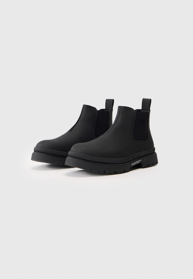 Zwarte Chelsea-boots van glad synthetisch materiaal, met een brede elastische zijpaneel, trekriem en een chunky rubberen zool met groeven.
