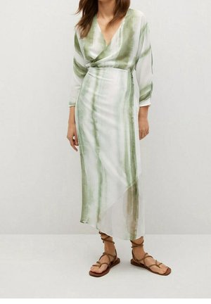 Mujer con un vestido largo cruzado de rayas verdes claras y blancas con mangas tres cuartos y sandalias planas marrones con cordones.